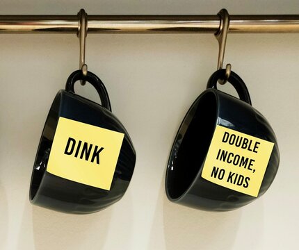 Two coffee cups with stick note written DINK acronym stands for Double Income, No Kids - referring to couples who are voluntarily childless