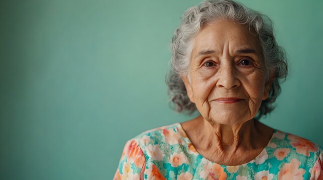 A full body portrait of a content and vibrant elderly Brazilian woman happily posing in a floral sundress against a plain sage background with ample copy space above the subject