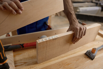 Male artisan worker holding and assembling pieces of wood using glue