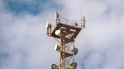 A tall tower with many antennas on top. The sky is cloudy and the sun is shining. The tower is a...