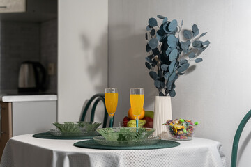 romantic dinner. There are green plates on the table, glasses with a drink, croissants, flowers in a white vase, fruits. setting the table for dinner. Soft lighting. The cozy atmosphere of the house.