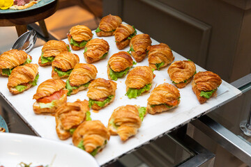 Tray of mini croissant sandwiches filled with lettuce and smoked salmon on buffet display