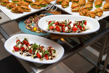 Plates of caprese salad with cherry tomatoes, mozzarella, arugula, and balsamic dressing on buffet display