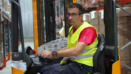 Mature expertise male worker using forklift in a storage warehouse