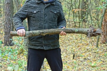 one aggressive man in stylish black jacket and pants holds heavy long grey wooden stick in front of...