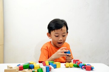 A young boy in an orange shirt focused on stringing colorful wooden beads, developing fine motor skills and creativity. Ideal for educational, childhood development, and playful learning concepts.