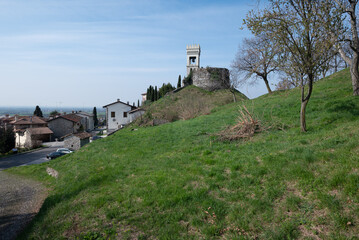 Slope down the hillside of the castle of Fagagna in summer, with parking lot with cars and a white house of the village on the hilltop