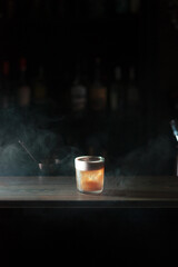 Cocktail with a foam standing on a bar counter, surrounded by smoke, close up view, vertical image 