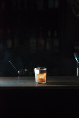 Cocktail with a foam standing on a bar counter, surrounded by smoke, close up view, vertical image 