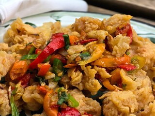 A plate of crispy fried chicken pieces topped with colorful garnishes including red chilies, green onions, and other vegetables