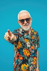 Naklejka premium Middle-aged man with white beard and glasses, wearing a patterned shirt and sunglasses, pointing to his right.