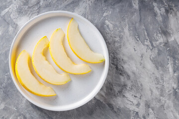 Fresh Melon Slices on White Plate against Grey Concrete Background, Top View, Copy Space