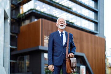 Naklejka premium Senior male entrepreneur with bag looking away and contemplating while standing against modern building