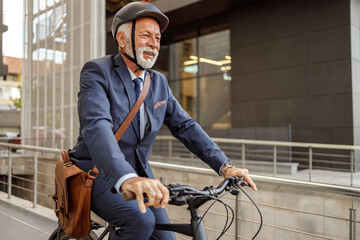 Positive male commuter with headwear and laptop bag riding bicycle to work on street in modern city