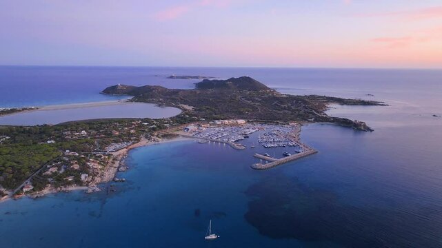 Aerial view at golden hour of Campulongu Bay in Villasimius, with calm waters, anchored boats, and iconic Torre di Porto Giunco.