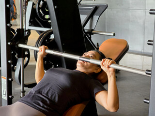 Beautiful Asian female athlete aged 40 years exercising to build muscle mass. lifting weights above his head on a bench press machine.
