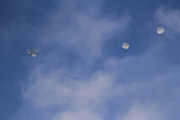 A small aircraft is seen in a bright blue sky, dispersing parachutes that drift downwards