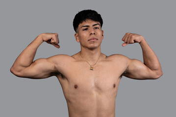 young latin man with naked torso showing biceps isolated on grey background