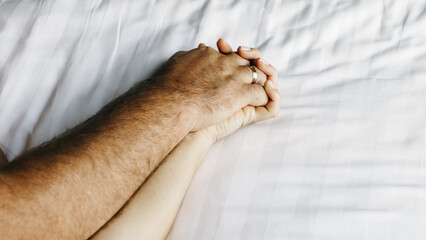 A close-up of a couple's hands intertwined on the bed, capturing a moment of relaxation and intimacy. This scene conveys the connection and pleasure in their loving relationship.