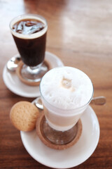 fresh hot latte with milk foam and iced espresso coffee drink with homemade biscuits cookies on wooden table in cafe