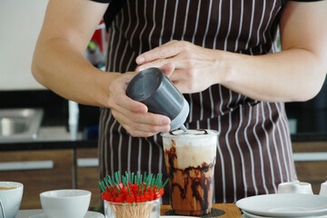 Close up on hand of barista man for pouring the chocolate into the iced coffee on counter bar in coffee shop