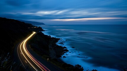 A lone car pauses at a lookout point along the road its lights adding a touch of warmth to the cool dark ocean below.