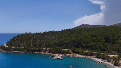 Fototapeta premium A quiet, secluded bay with small boats docked along the shore, surrounded by lush forested hills and clear turquoise water under a bright sky. 