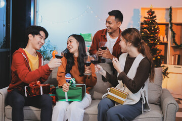 Group of young Asian man and women as friends having fun at a New Year's celebration, holding gift boxes standing by Christmas tree decoration, midnight countdown Party at home with holiday season.