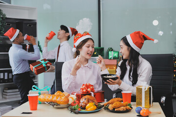 full length view of a group of business team wearing red Santa hat and exchange gift box together in the office for Christmas.