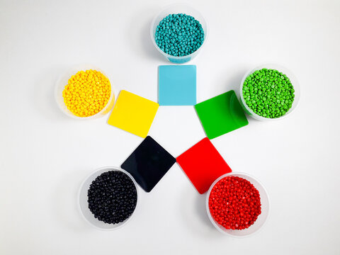 Various colors of masterbatch granules in a cup equipped with color chips as examples of the resulting colors, isolated on a white background. Polymers carrying color pigments in the plastics industry