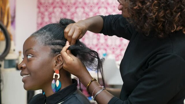 Hairdresser making crochet braids to a smiling client in an afro hair salon while talking and laughing