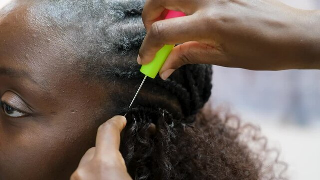 Hairdresser making crochet braids to a smiling customer in an afro hair salon