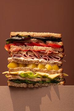 Giant layered rainbow sandwich with variety of fillings on neutral background.