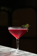 Classic martini glass cocktail with branch. Red alcoholic beverage on a marble table and dark background with copy space