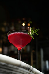 Classic martini glass cocktail with branch. Red alcoholic beverage on a marble table and dark background with copy space