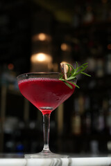Classic martini glass cocktail with branch. Red alcoholic beverage on a marble table and dark background with copy space