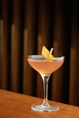 Bronx cocktail glass with orange peel slice on a wooden bar counter, background with copy space