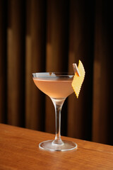 Bronx cocktail glass with orange peel slice on a wooden bar counter, background with copy space