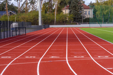 Nowa bieżnia lekkoatletyczna na szkolnym stadionie sportowym w słoneczny jesienny dzień. Nowo wybudowany i otwarty szkolny stadion sportowy - bieżnia z nawierzchnią wykonaną ze specjalnego tworzywa.