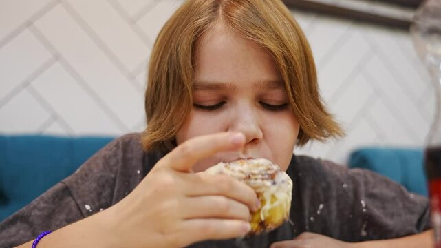 close-up. teen girl bites and chews cinnamon bun. Dessert snack in the shopping center.