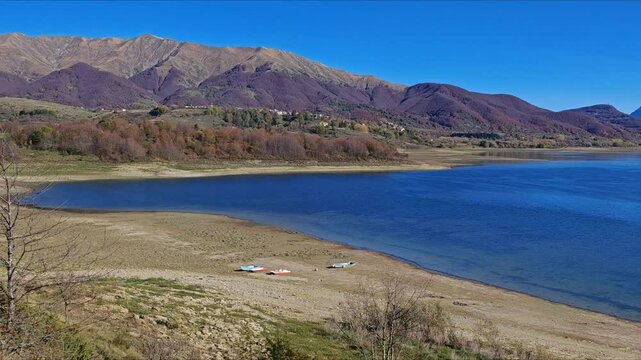 A serene autumnal scene of Campotosto lake with high mountains in the background during sunny day of october, abruzzo region, Italy