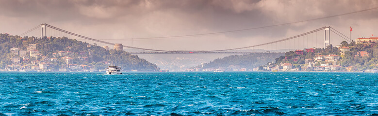 Naklejka premium A panoramic view of the Bosphorus in Istanbul, where the serene blue waters meet the horizon, with a bridge and boats dotting the landscape