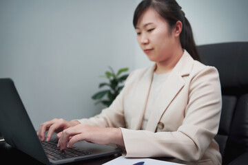 Woman typing work on laptop and checking work on paper as well