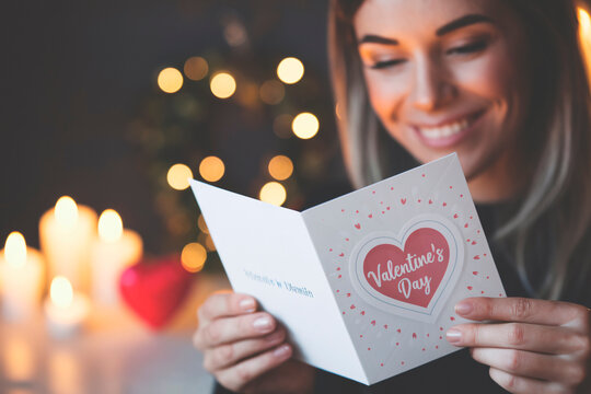Young Woman Reading Valentine's Day Card with Tender Smile. Romantic portrait of a beautiful young woman holding and reading a Valentine's Day greeting card with a gentle smile. 