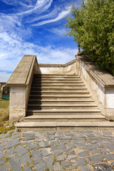 Wide concrete stairs with concrete railing. Old stairs with stone surface. Castle stairs, climb, step, castle, monuments. Blue sky with white clouds. Stone paving.