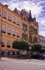 Square with Historic building with decorative elements. Paved square with trees in front of buildings and parked cars.