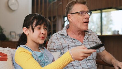 Grandfather and granddaughter together watch interesting entertainment media on TV. Old senior use technology communicate with young generation cross generation gap strengthen family bond. Divergence.