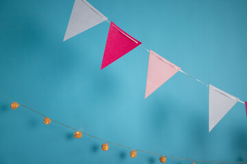 Close-up of festive triangle bunting in pink, red, and white colors alongside warm string lights against a bright blue background.