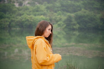 A woman in a yellow jacket stands by a lake