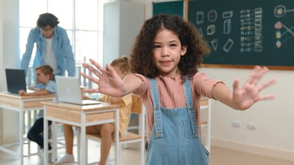 American girl looking at camera while waving hand to greeting. Group of diverse elementary student studying coding engineering prompt and generating AI or programing software. Education. Pedagogy.
